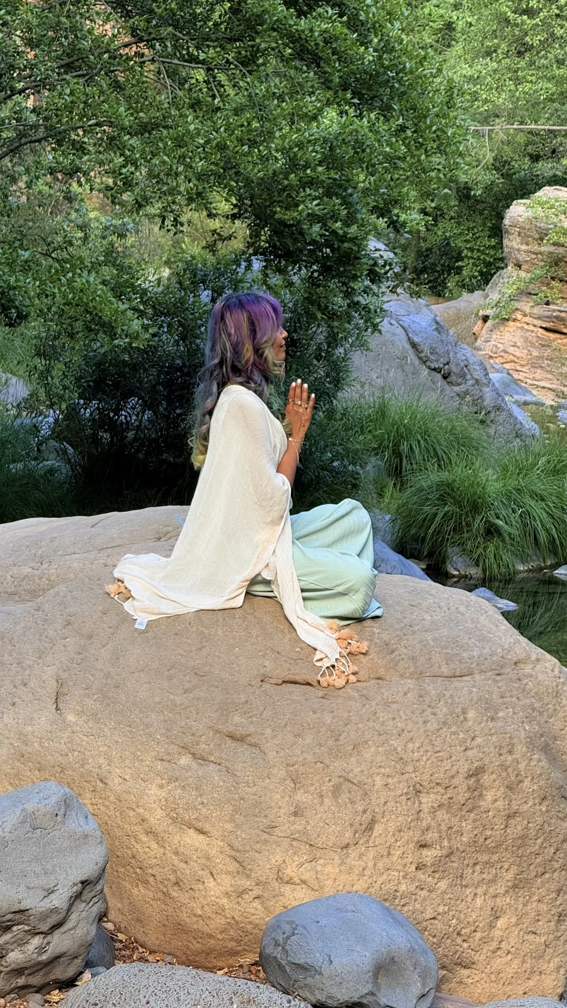 Zineea sitting in stillness on a rock beside a stream
