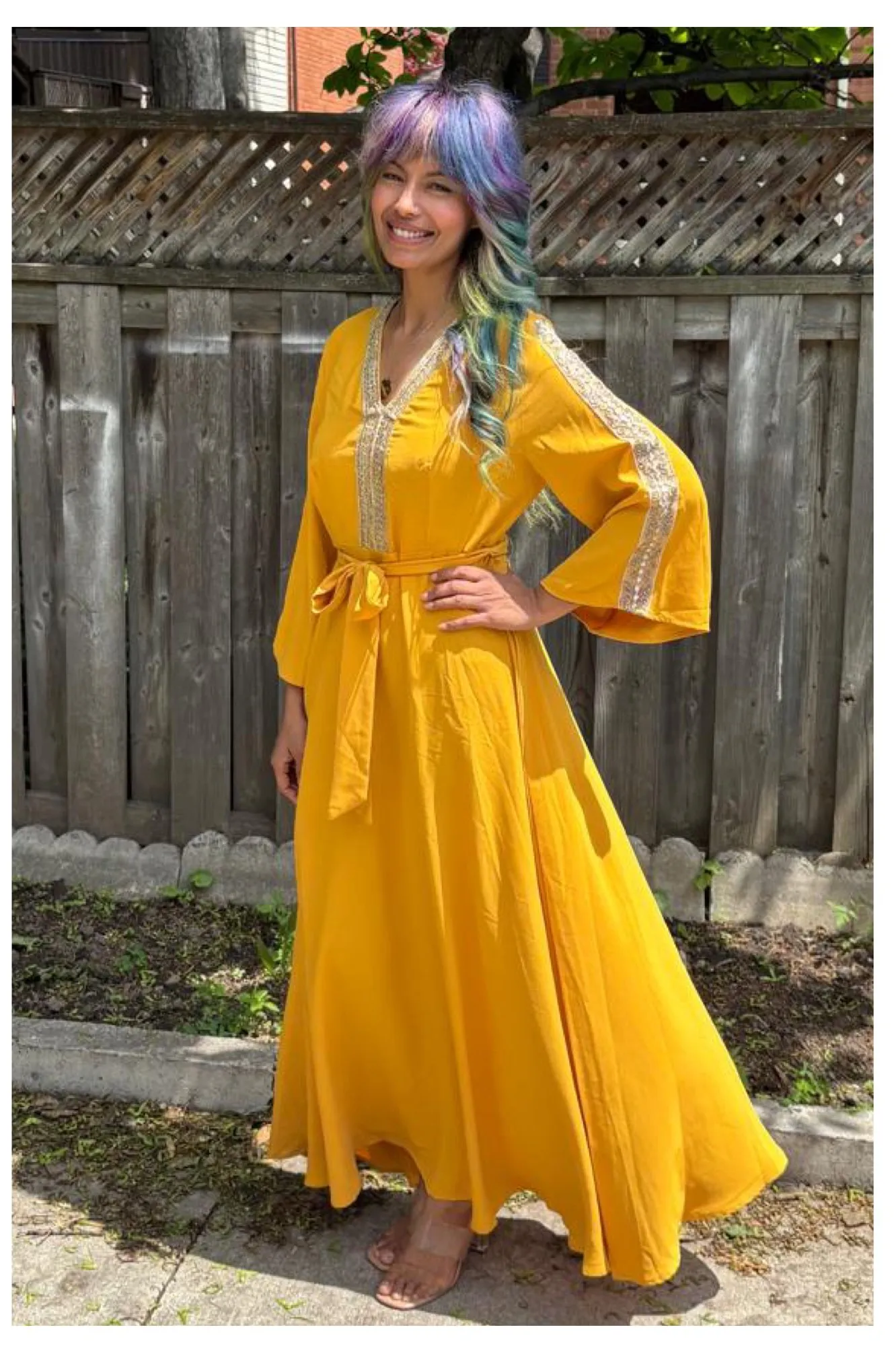 Zineea standing in a garden in a long yellow dress, smiling